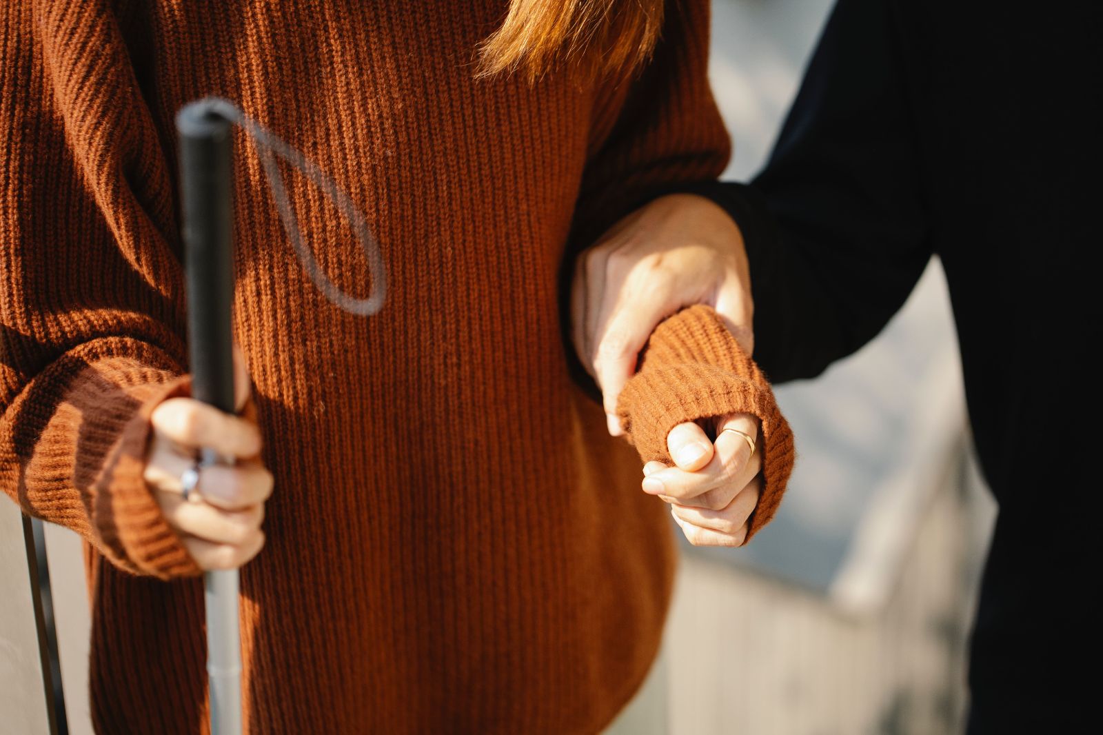Blind woman walking with cane. hand on her forearm guiding her towards the camera.