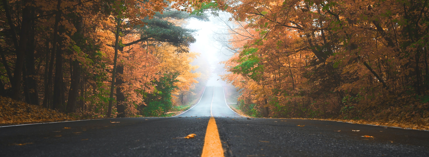 A woman sits at a table in a coffee shop. She is smiling big at something outside of the frame. She is holding a coffee in a to go cup. Her left arm is a prosthetic.