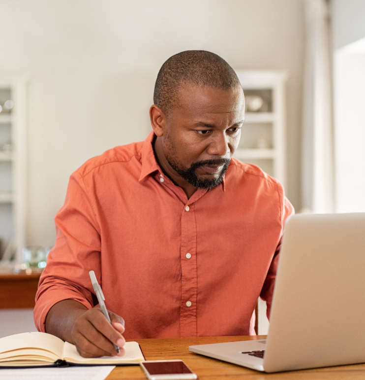 a man taking note while looking at his laptop