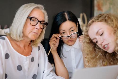 A group of three women sit around a laptop. They are gesturing to and looking intently at something on the screen