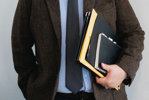 A close up of a man holding files and a notebook.