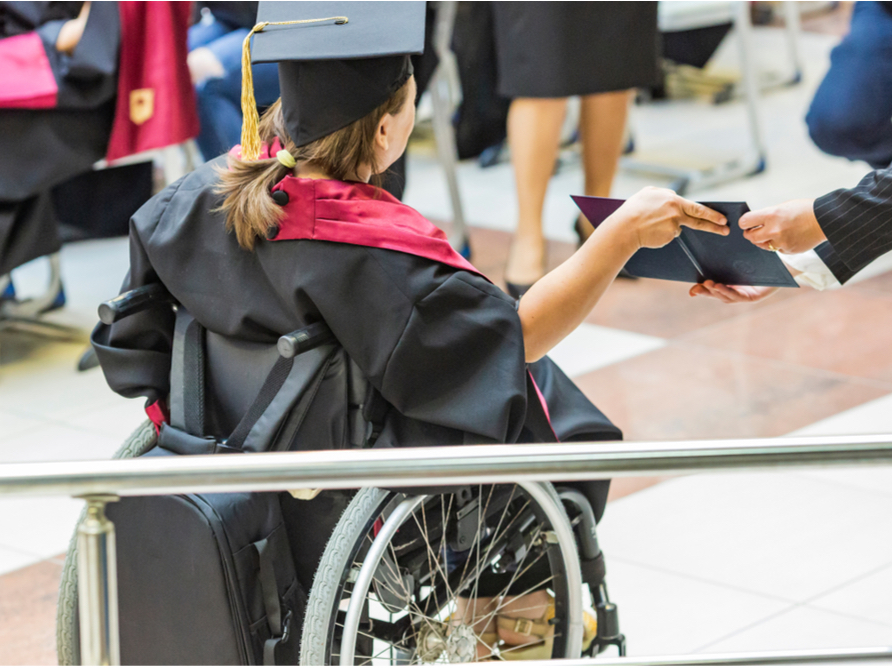 A photo of a person using a wheelchair receiving a diploma. They are dressed in a graduation cap and gown.
