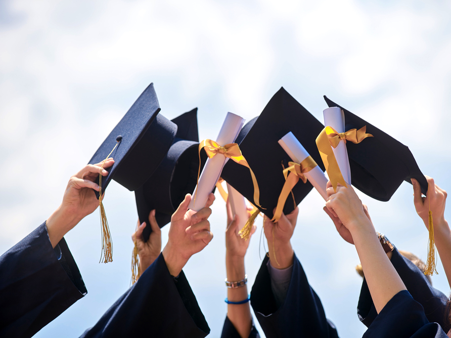 A photo of hands lifting up diplomas and graduation caps toward the sky.