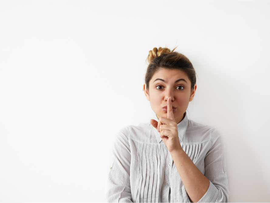 A photo of a woman with her pointer finger to her lips, indicating to be quiet.