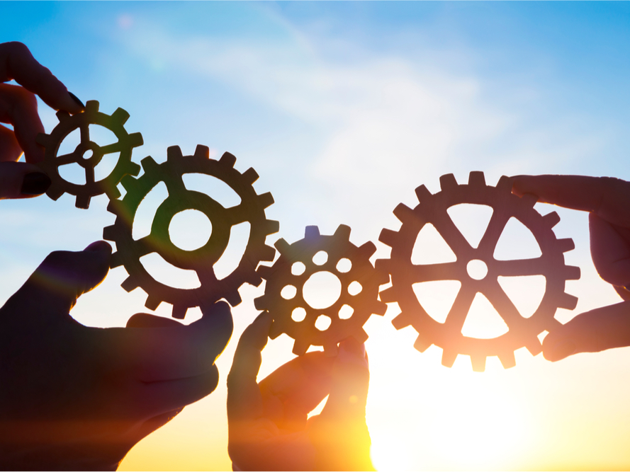 A photo of four hands holding up gears 