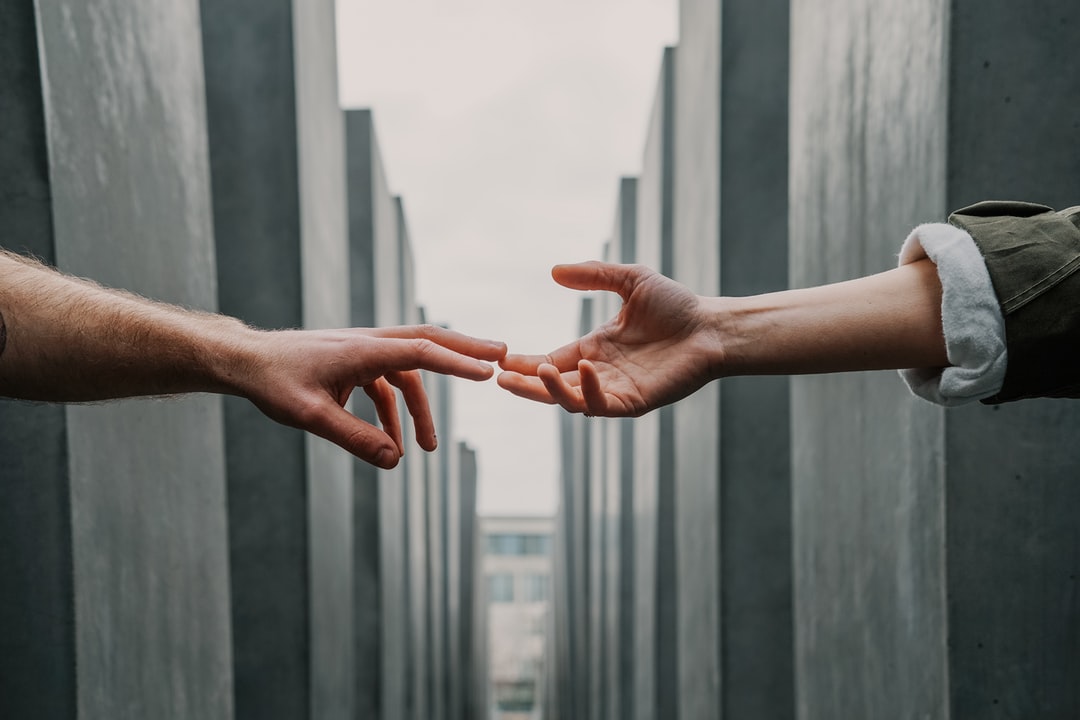 A photo of two hands reaching toward each other. Their fingertips are barely touching.
