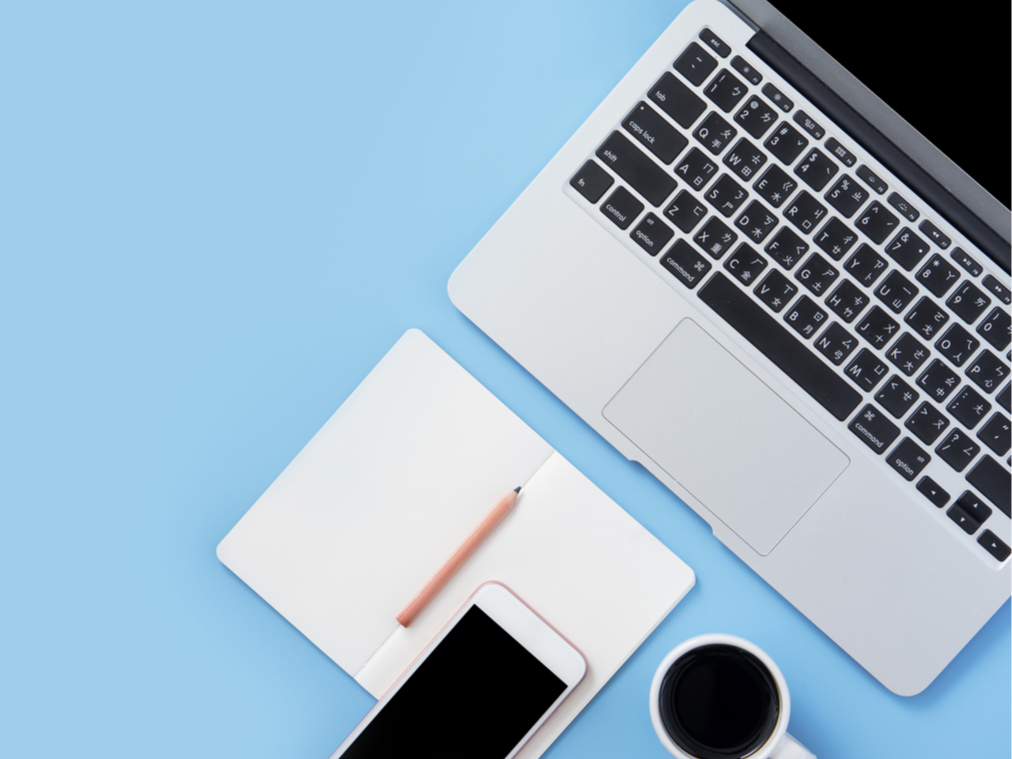 A photo of a laptop, phone, notebook, pencil, and cup of coffee on a desk.