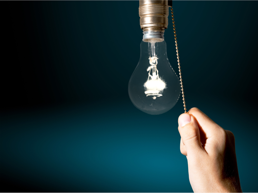 A closeup photo of a hand pulling a cord to turn on a hanging lightbulb 