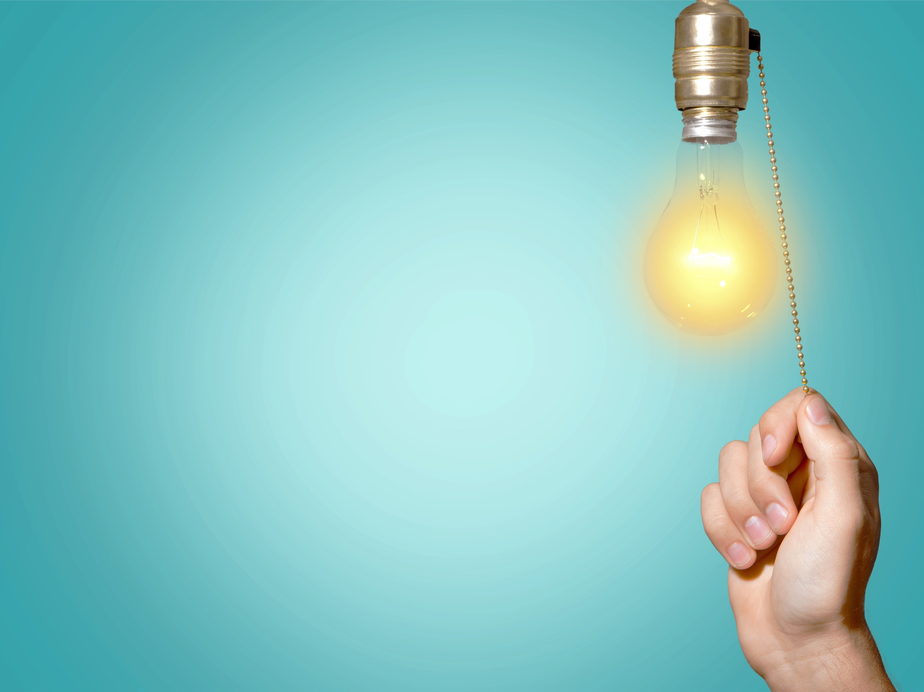 A closeup photo of a hand pulling a cord to turn on a hanging lightbulb 