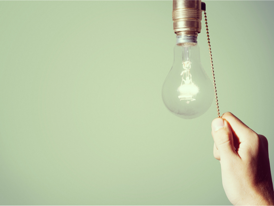 A closeup photo of a hand pulling a cord to turn on a hanging lightbulb 