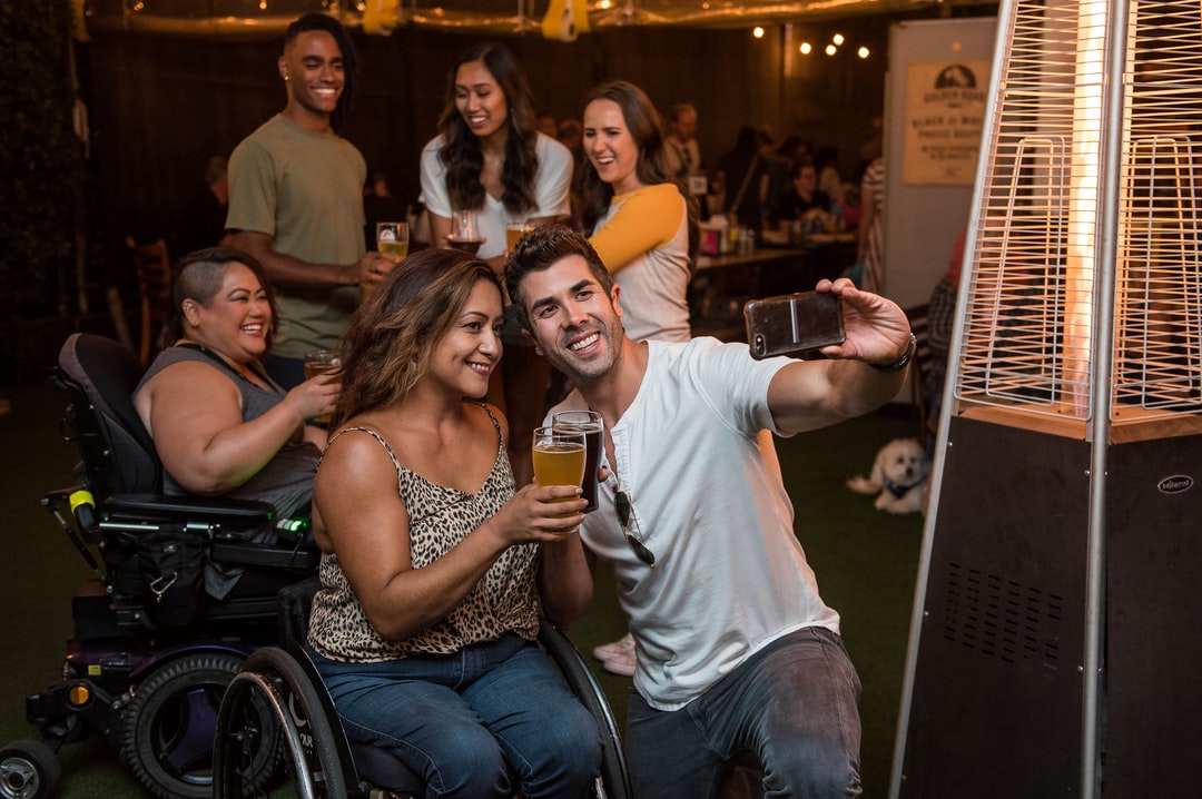 A photo of a group of people in a bar taking a selfie. Two of the group members are sitting in wheelchairs.