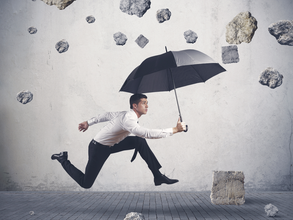 An image of a man holding an umbrella. There are large rocks falling from the sky.
