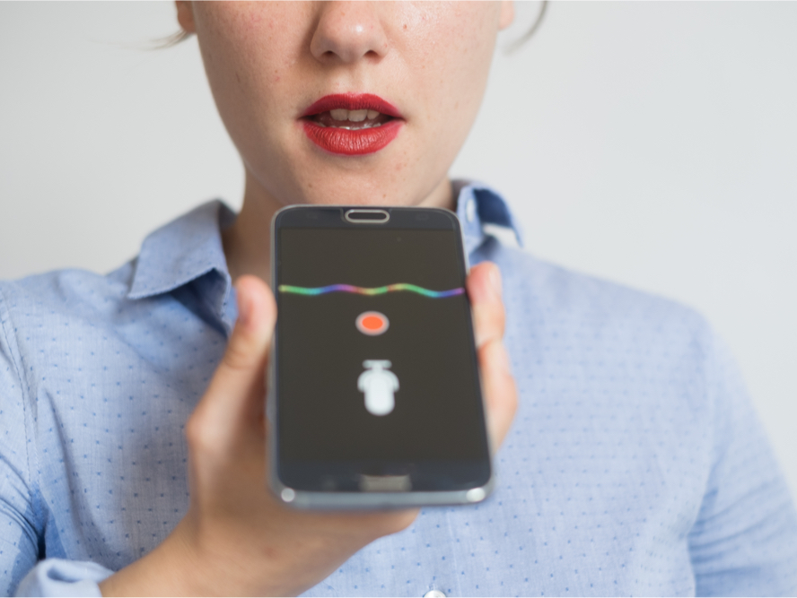 A photo of a woman holding her phone out in front of her and speaking into the mic.