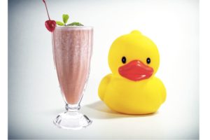 Image of a milkshake in a glass next to a large yellow bathtub rubber duckie