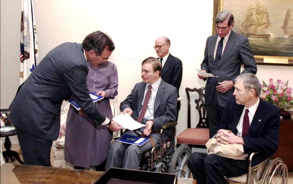 Image of man with a mustache sitting in a wheelchair shaking hands with President George HW Bush