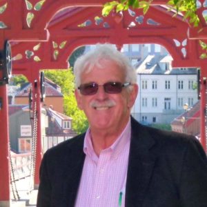 Smiling older man with white hair wearing sunglasses and posing in front of a red arch.