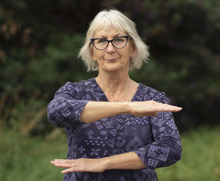 Image of older woman with white hear holding her arms in the shape of an equal sign.