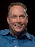 Long Description A smiling man in a blue shirt looks directly into the camera