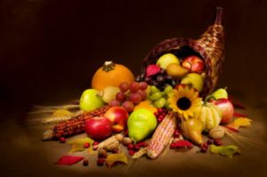 Image of cornucopia overflowing with fall holiday fruits and vegetables including pumpkins and sunflower