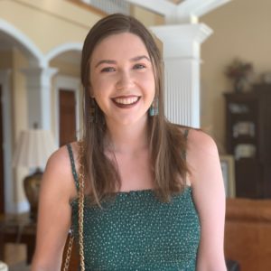 Young Caucasian woman with long light brown hair, wearing a thin strap polka dot green dress and gold chain purse.
