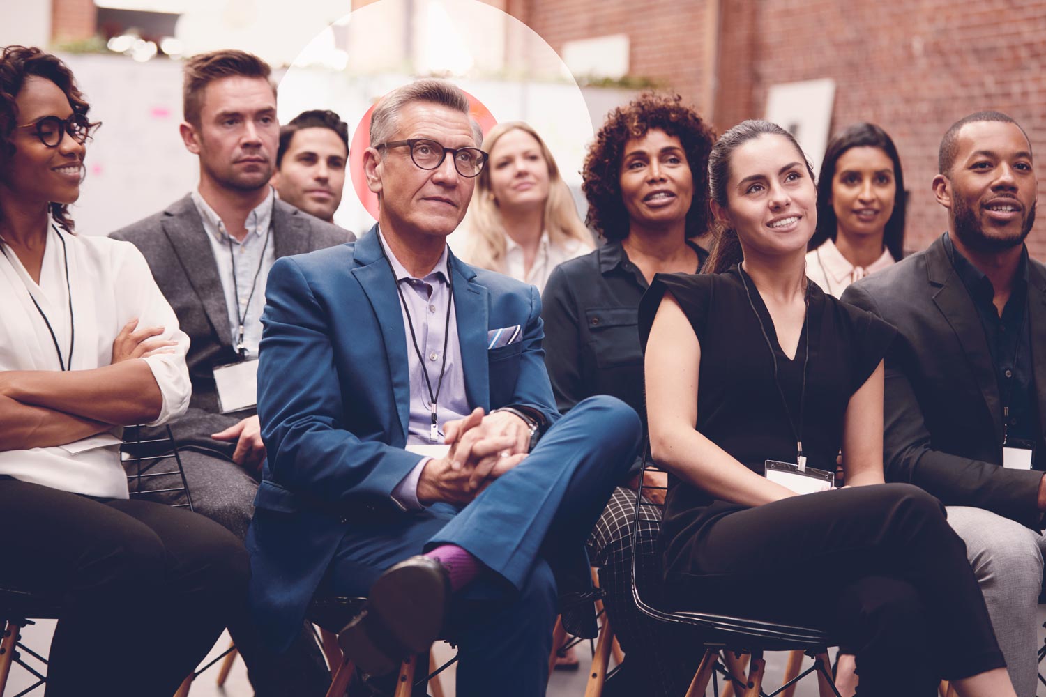 Image shows a group of business people sat on chairs, listening to a talk