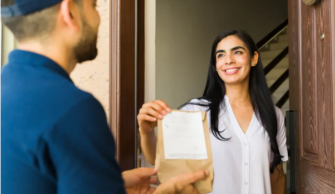 Woman receiving pills in brown paper bag from courier at her front door.