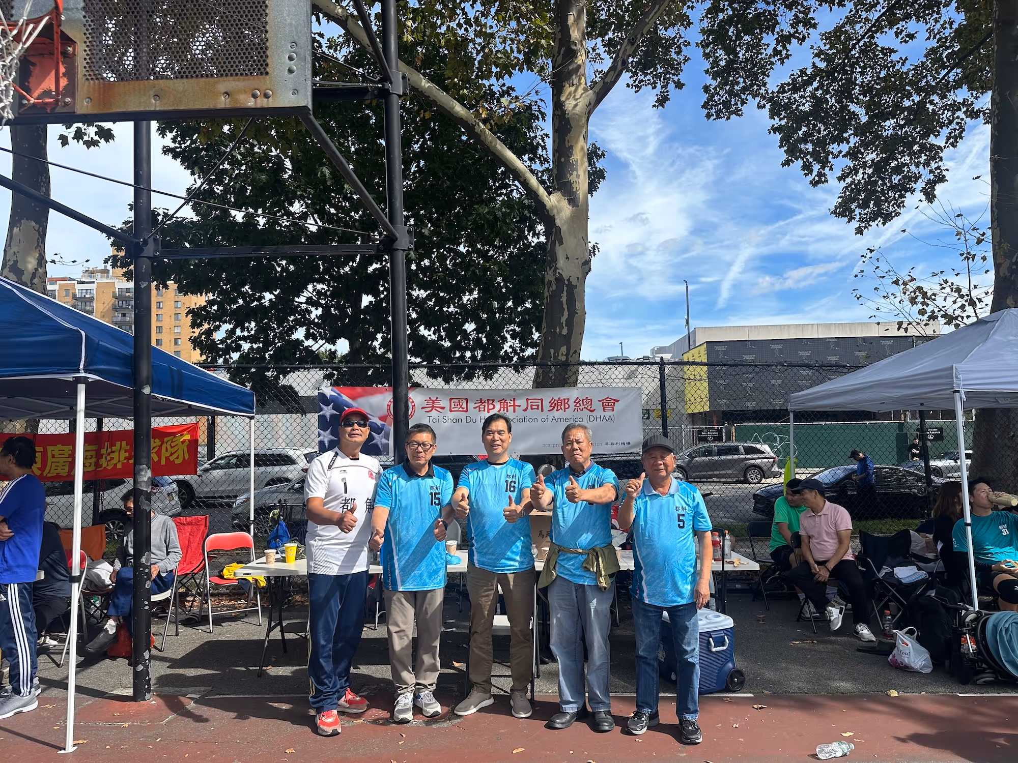 Man in plaid shirt speaks to an attentive audience at a casual, outdoor gathering with wooden decor and string lights, creating a warm atmosphere.