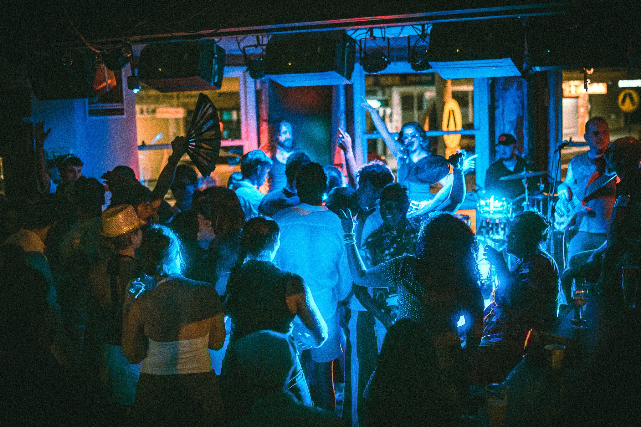 LUXE Crowded indoor concert with people dancing under blue and warm stage lighting, musicians playing instruments in the background.