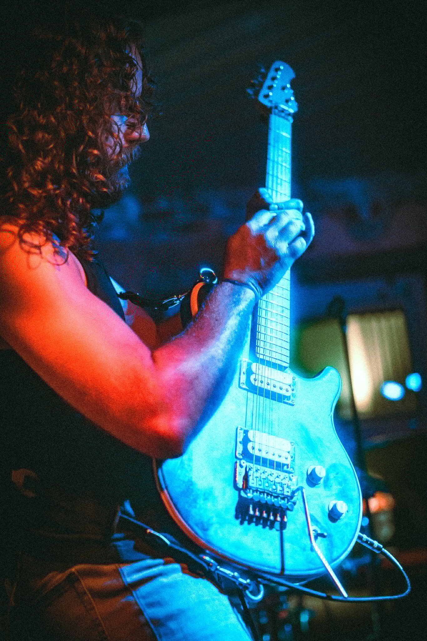 Man with curly hair playing an electric guitar under blue stage lighting. LUXE 