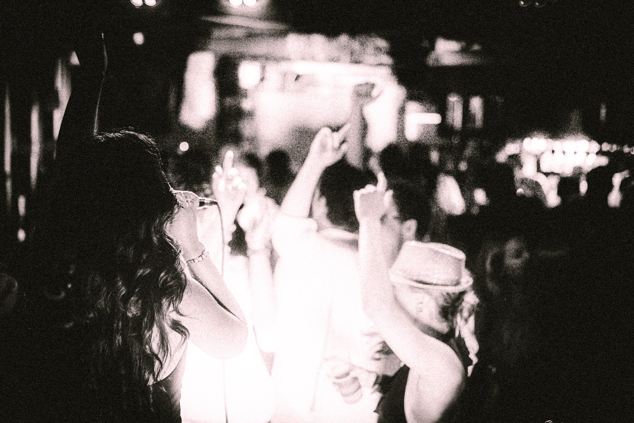 Black and white photo of a LUXE female singer with long hair performing to a lively crowd with raised hands.