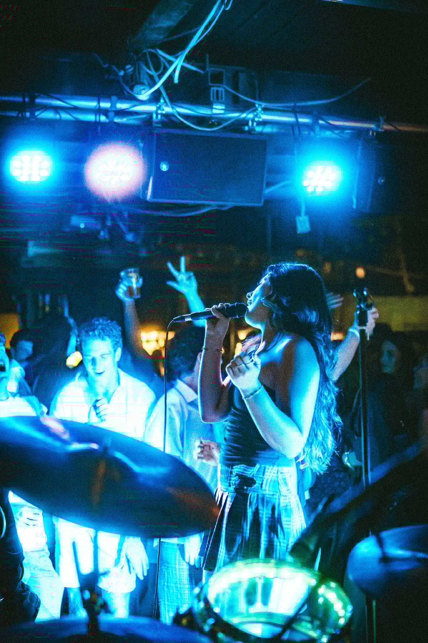 LUXE Female singer performing with a microphone on stage under blue lighting, with an audience enjoying the music.