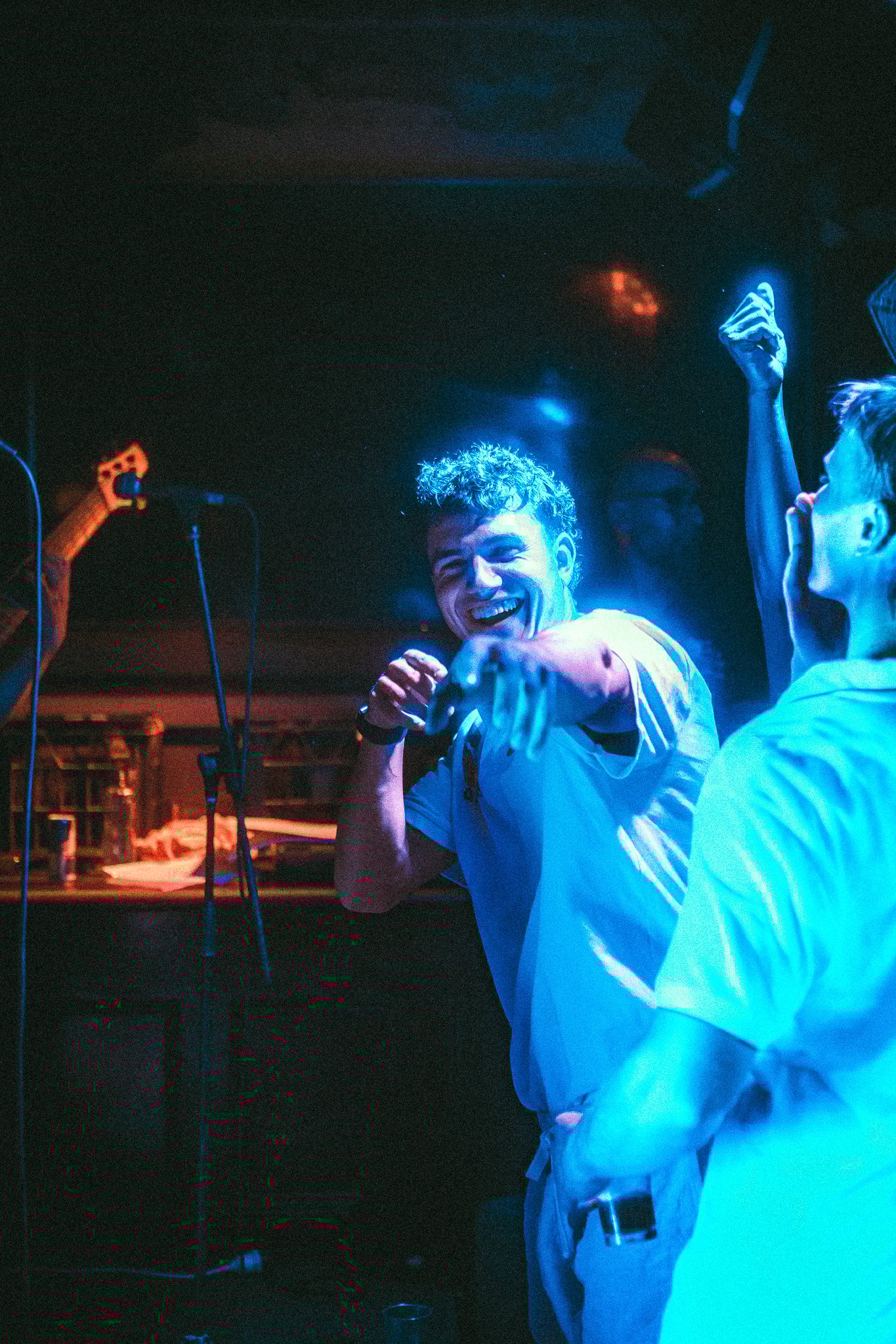 Young man smiling and pointing toward the camera in a dimly lit blue-toned party setting. LUXE 