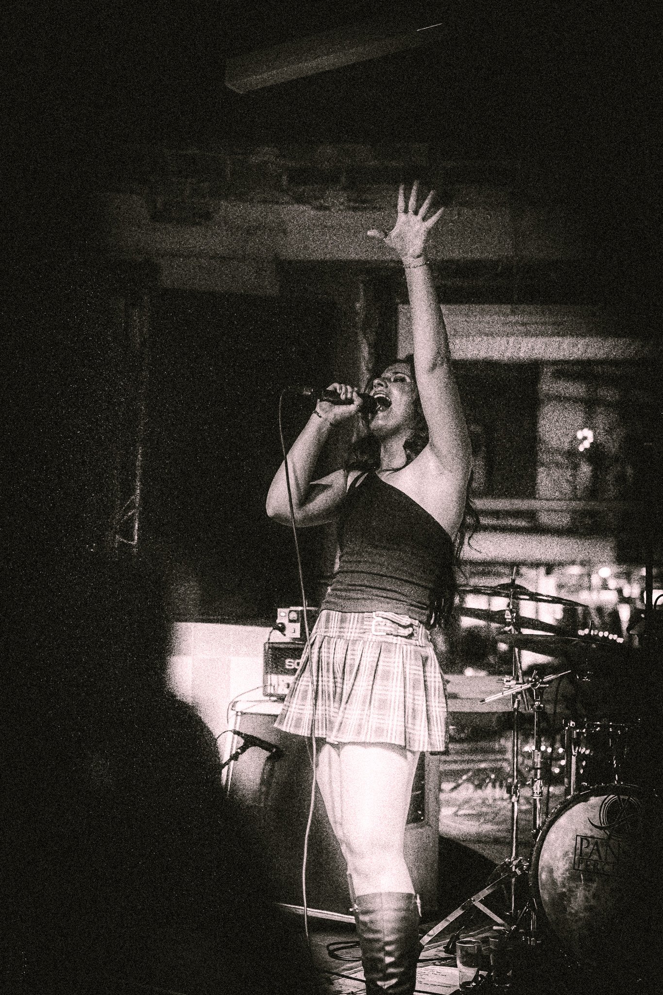 LUXE Female singer passionately performing on stage with one arm raised, wearing a plaid skirt and boots.