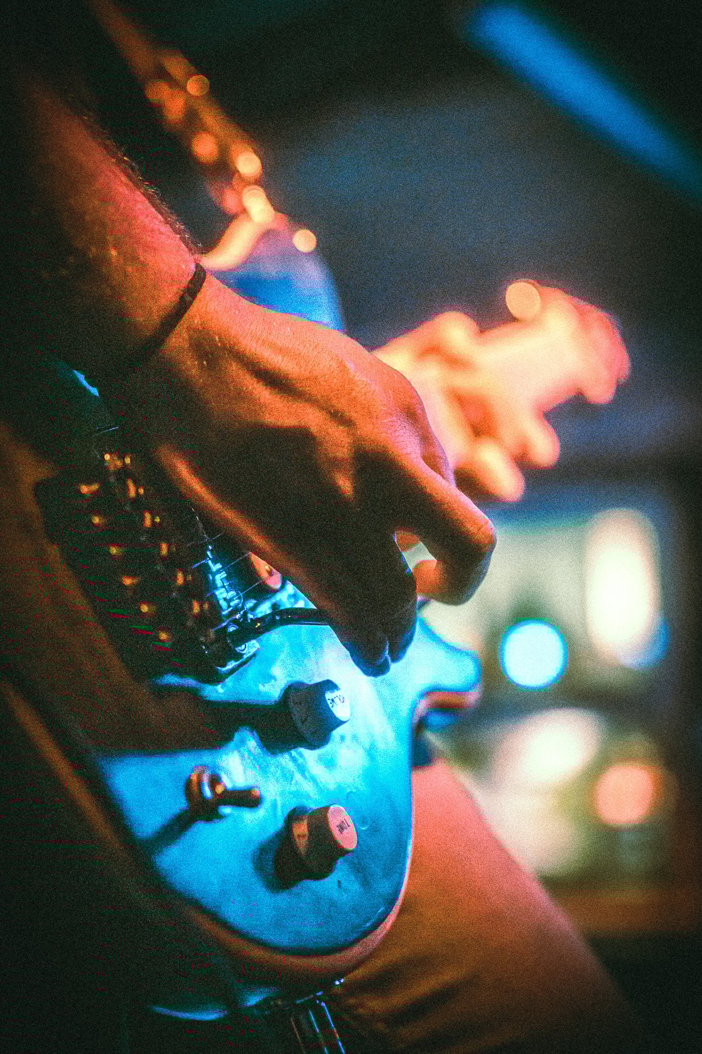 Close-up of a LUXE  hand playing an electric guitar with blurred colorful lights in the background.