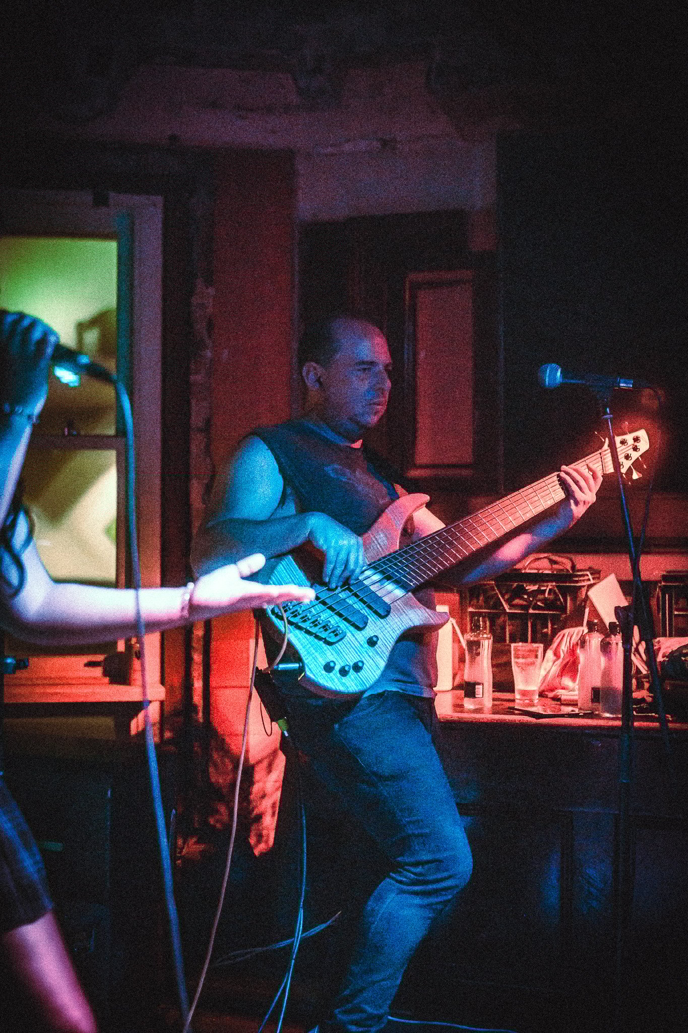 LUXE Man playing electric bass guitar on stage with colorful lighting and microphone nearby.