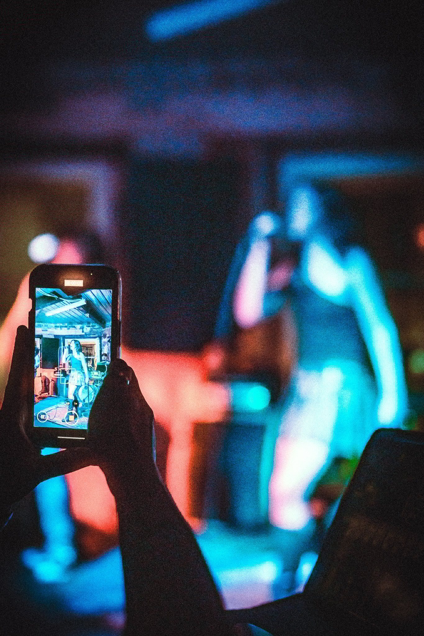 Person holding a phone recording LUXE  female singer performing on stage under blue and red lighting.