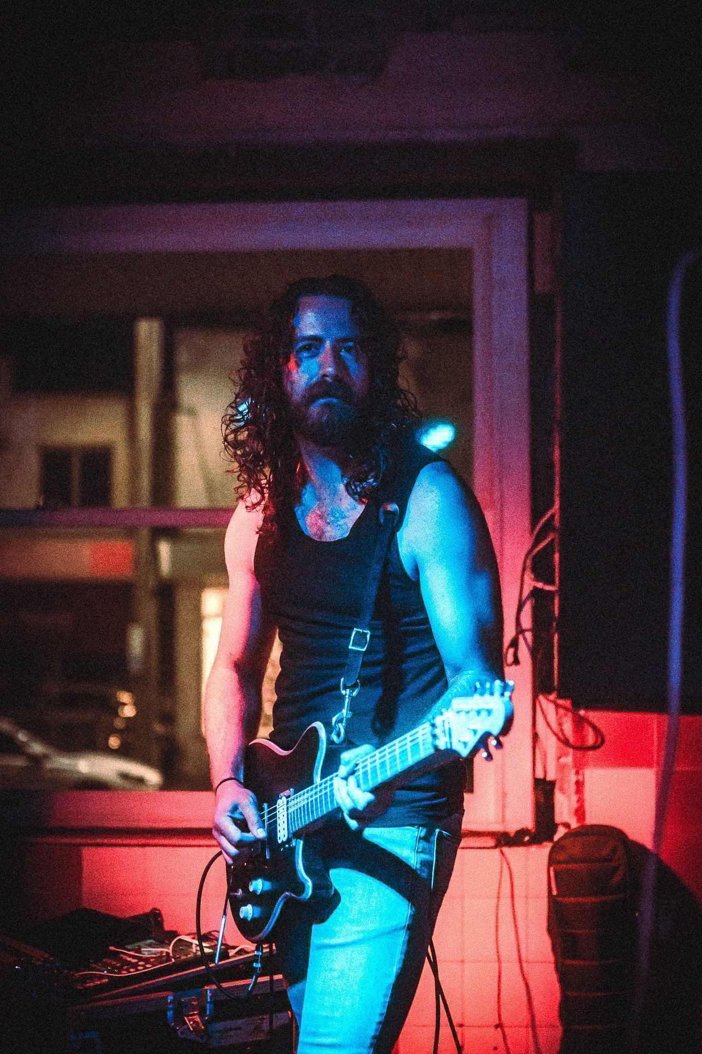 LUXE  Man with curly hair and beard playing electric guitar under blue and red stage lights.