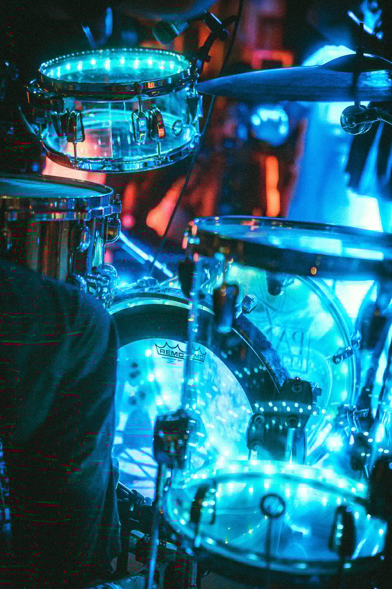 Close-up of a drum set illuminated with blue stage lights during a performance. LUXE 
