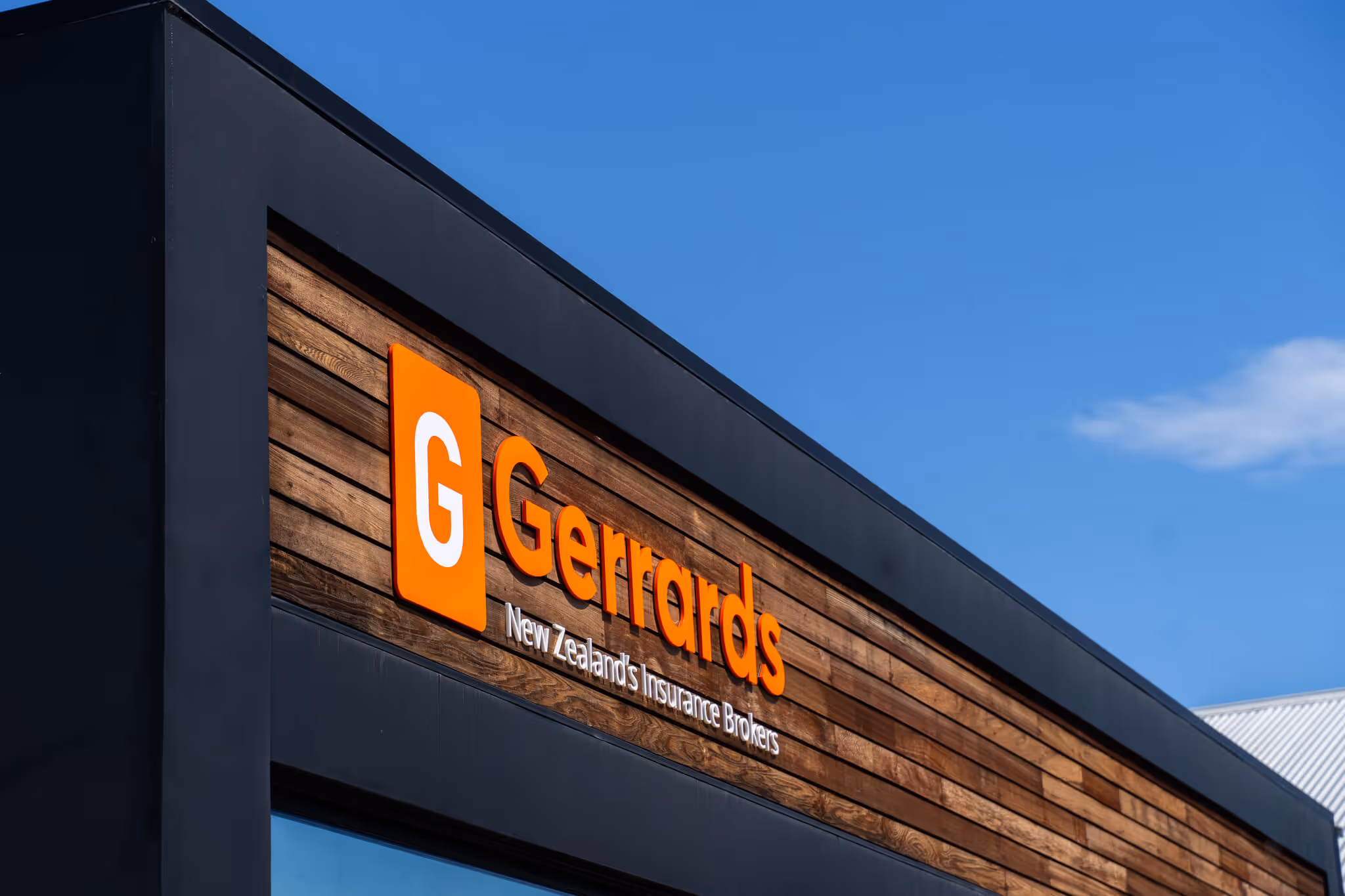 Exterior sign of Gerrards, New Zealand's Insurance Brokers, on a wooden and black building facade under a blue sky.