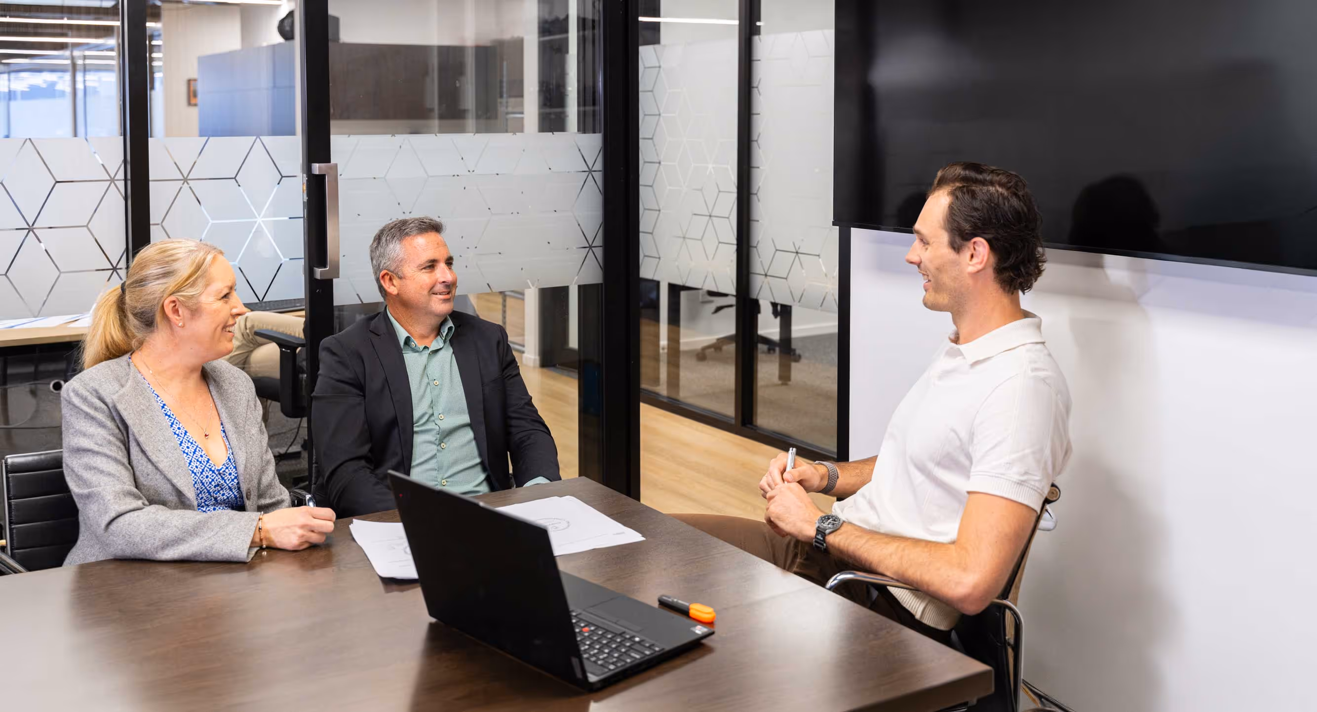 Three people having a meeting in a modern office with a laptop and documents on the table.