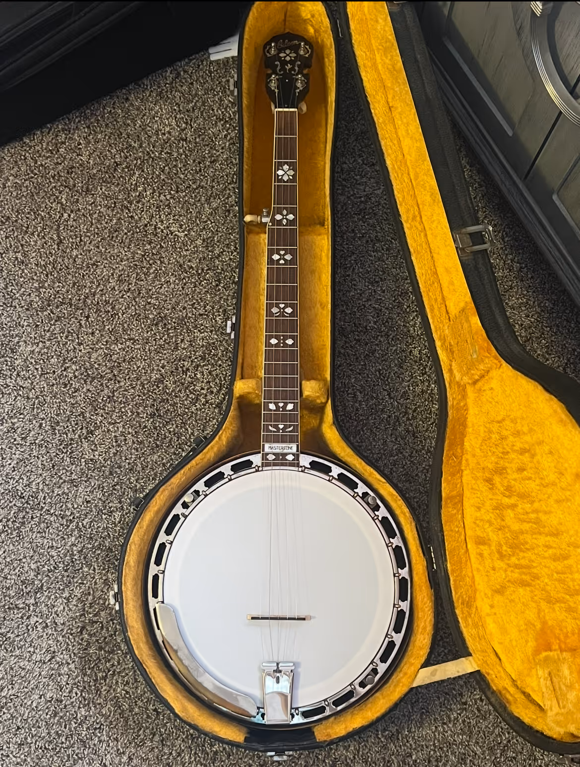 Open case with a Gibson Mastertone banjo featuring decorative inlays on the fretboard.
