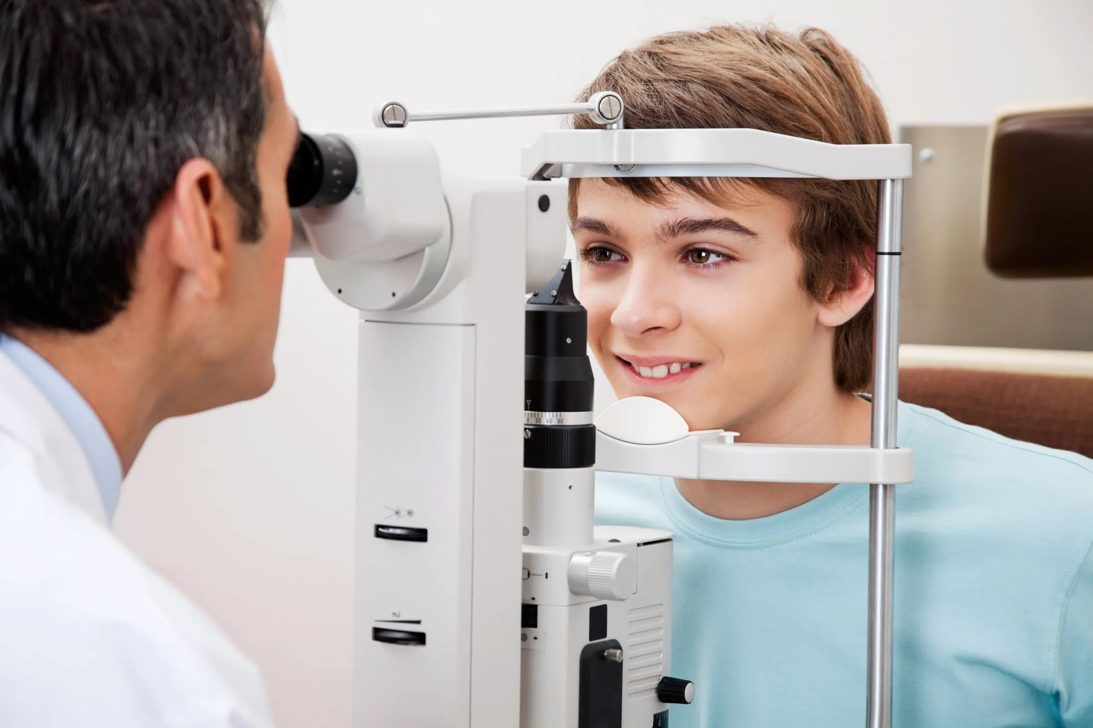 Boy smiling during an eye exam using a slit lamp with an optometrist.