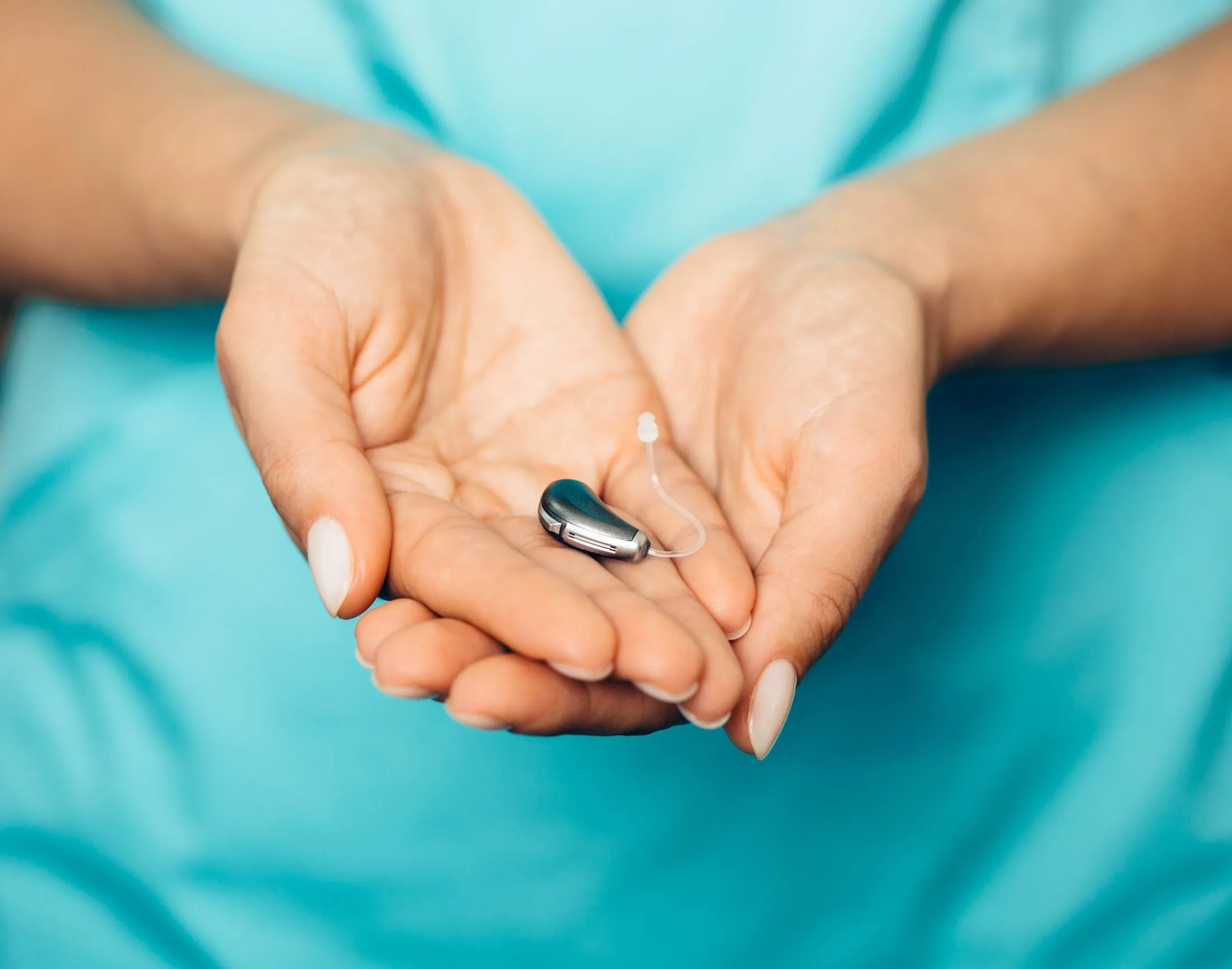 Hands holding a small modern behind-the-ear hearing aid device.