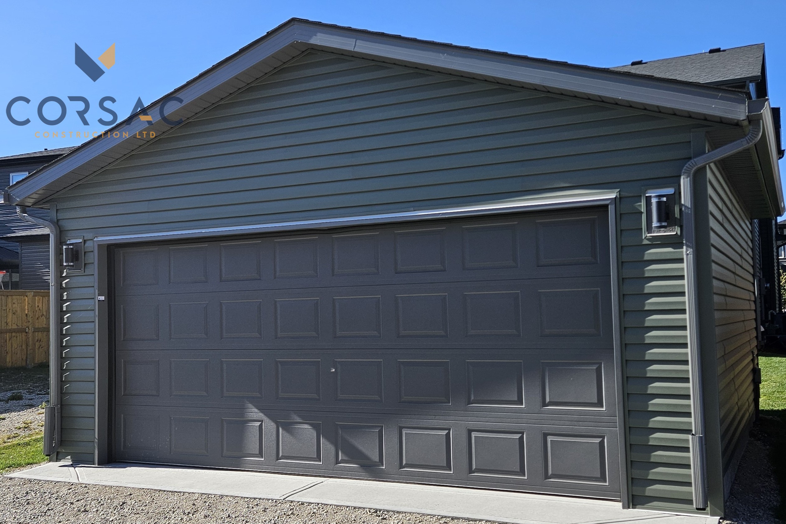 Grey garage door on a green-sided detached garage under a clear blue sky.