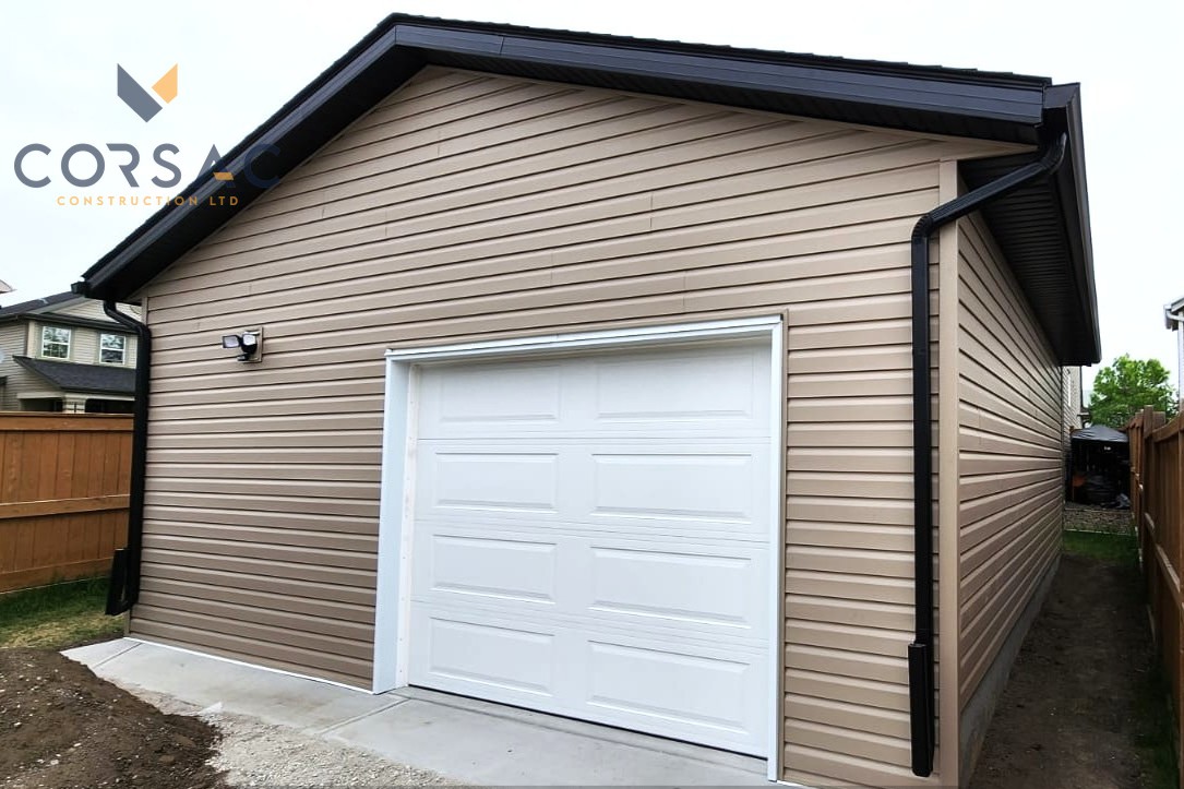 Beige detached garage with a white garage door, black gutters, and a security light on the left side.