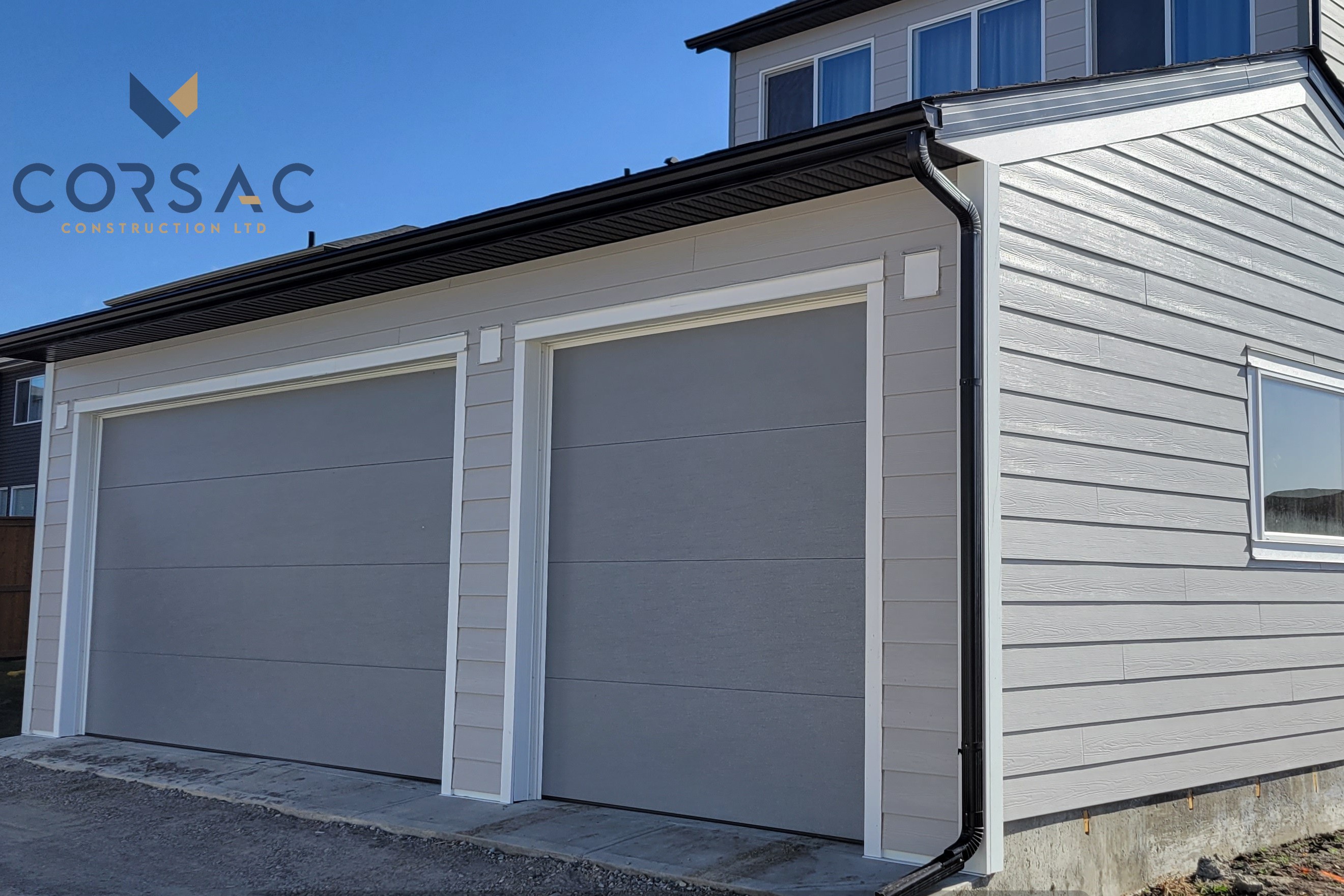 Modern house exterior with two closed gray garage doors and beige siding under a clear blue sky.