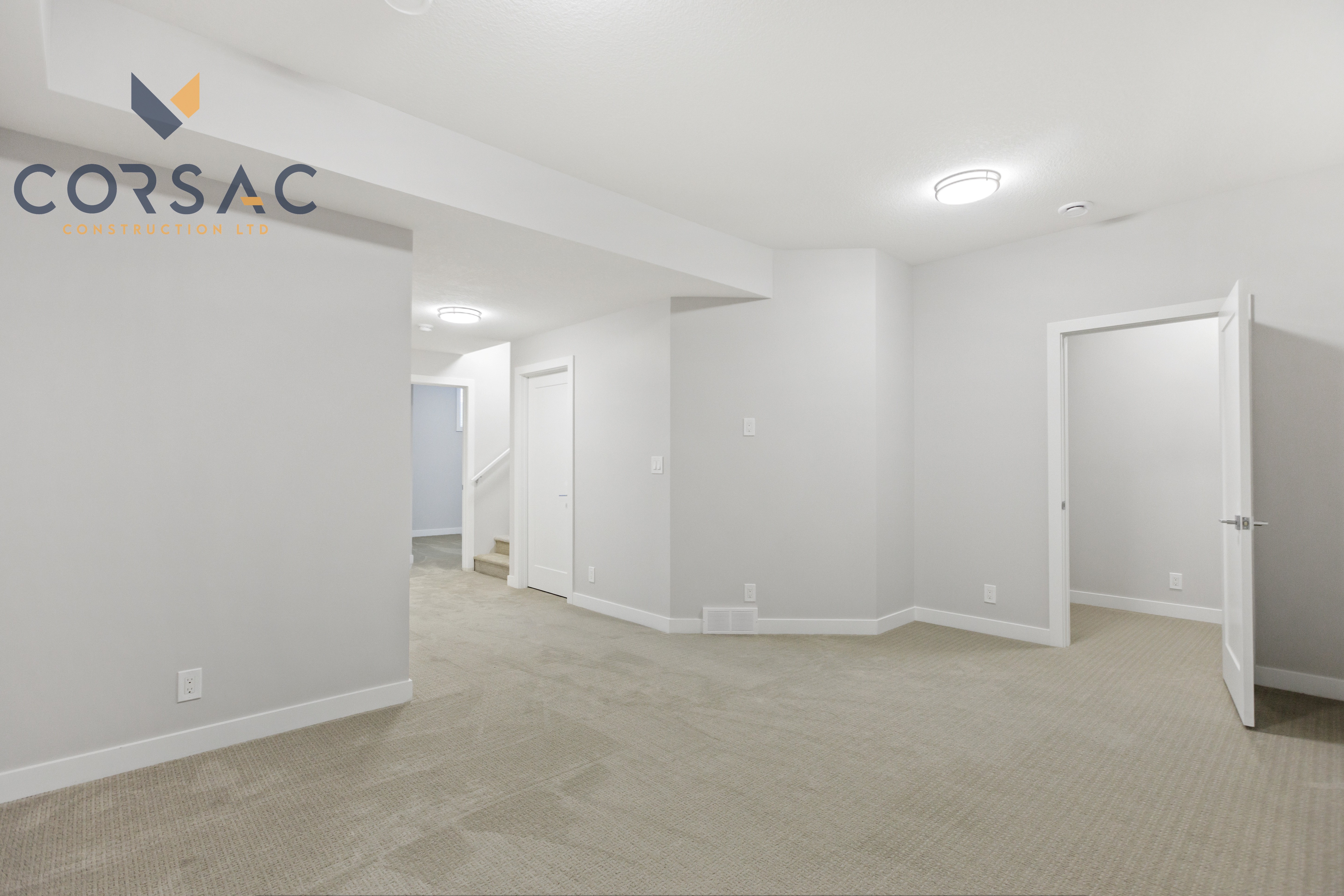 Empty basement room with beige carpet, white walls, stairs leading up, and an open doorway to another room.