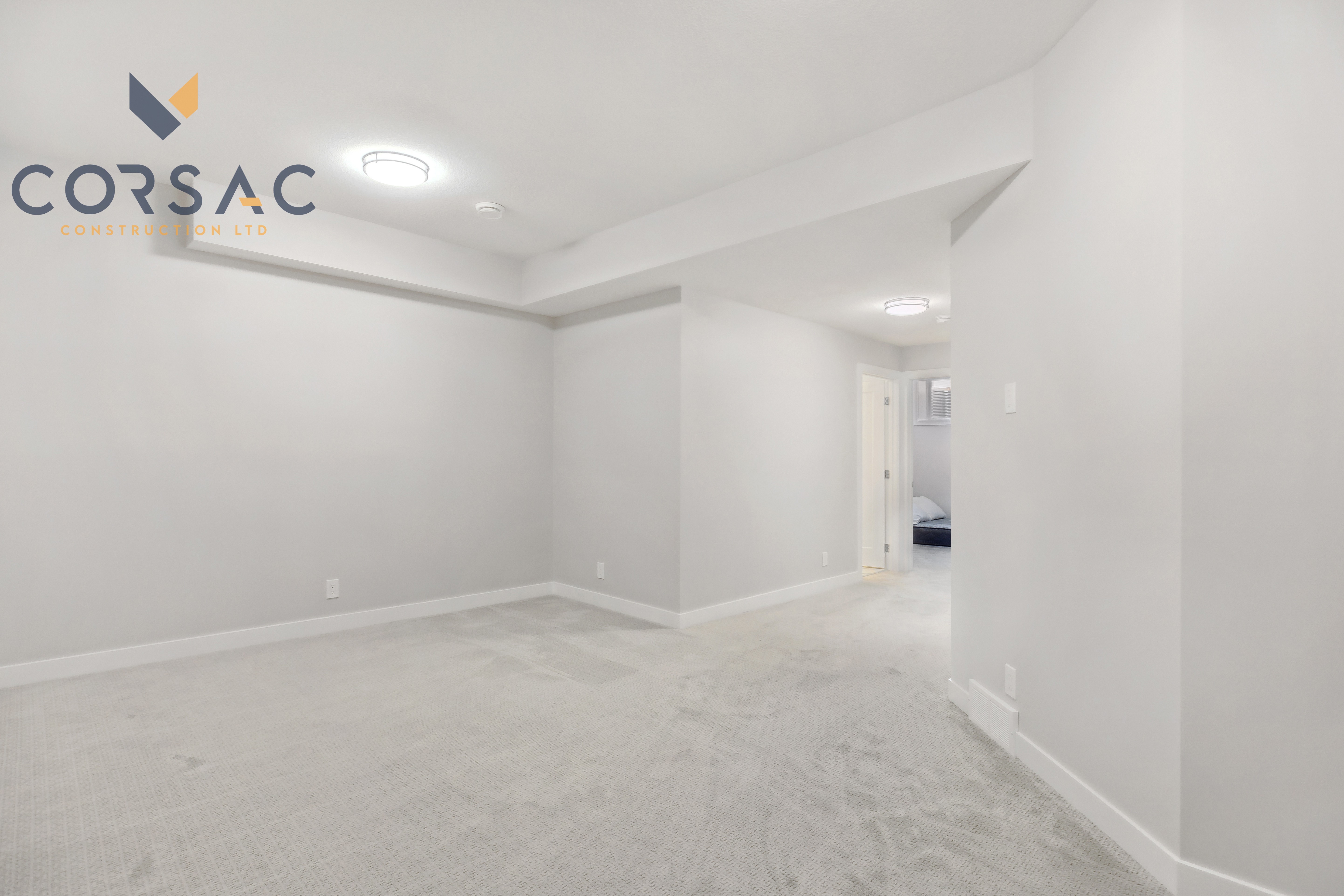 Empty basement room with light gray walls, carpeted floor, and ceiling lights.