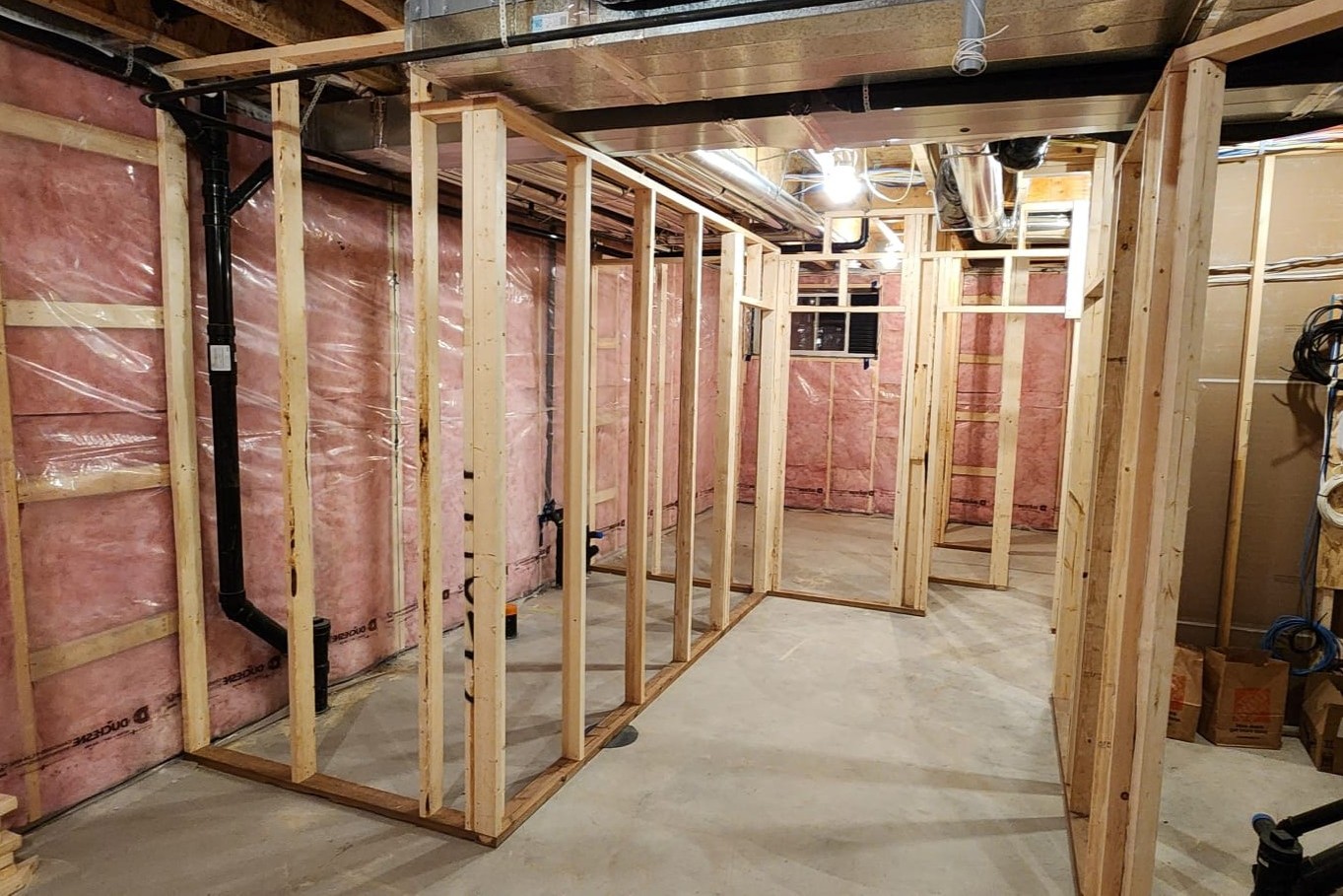Basement under construction with wooden framing for walls and pink insulation on the exterior walls.
