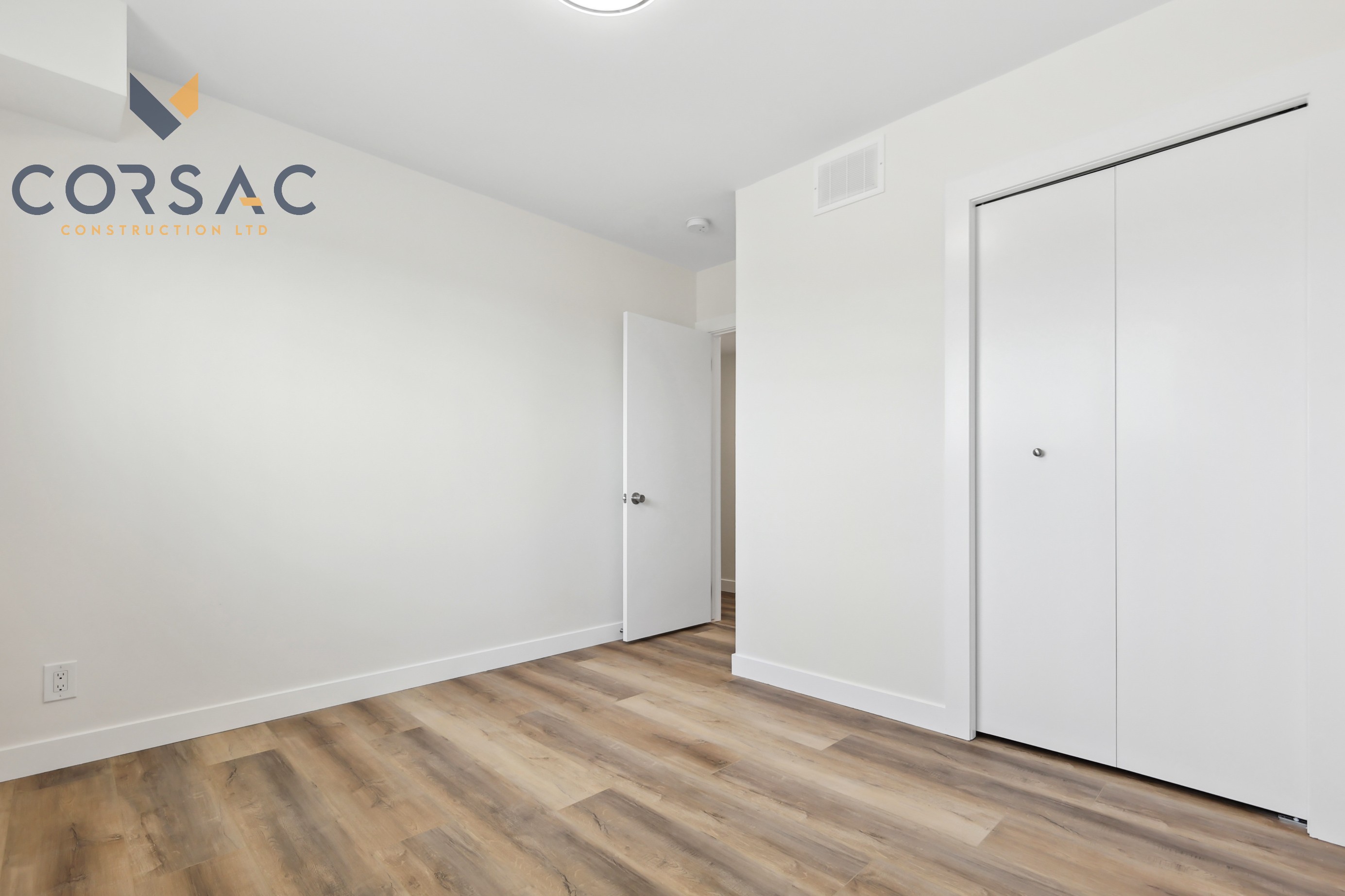 Empty room with white walls, wood flooring, an open door, and a closed closet with sliding doors.